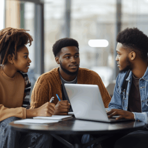 Three college students in a group meeting in a bright space. One student takes notes on a laptop.